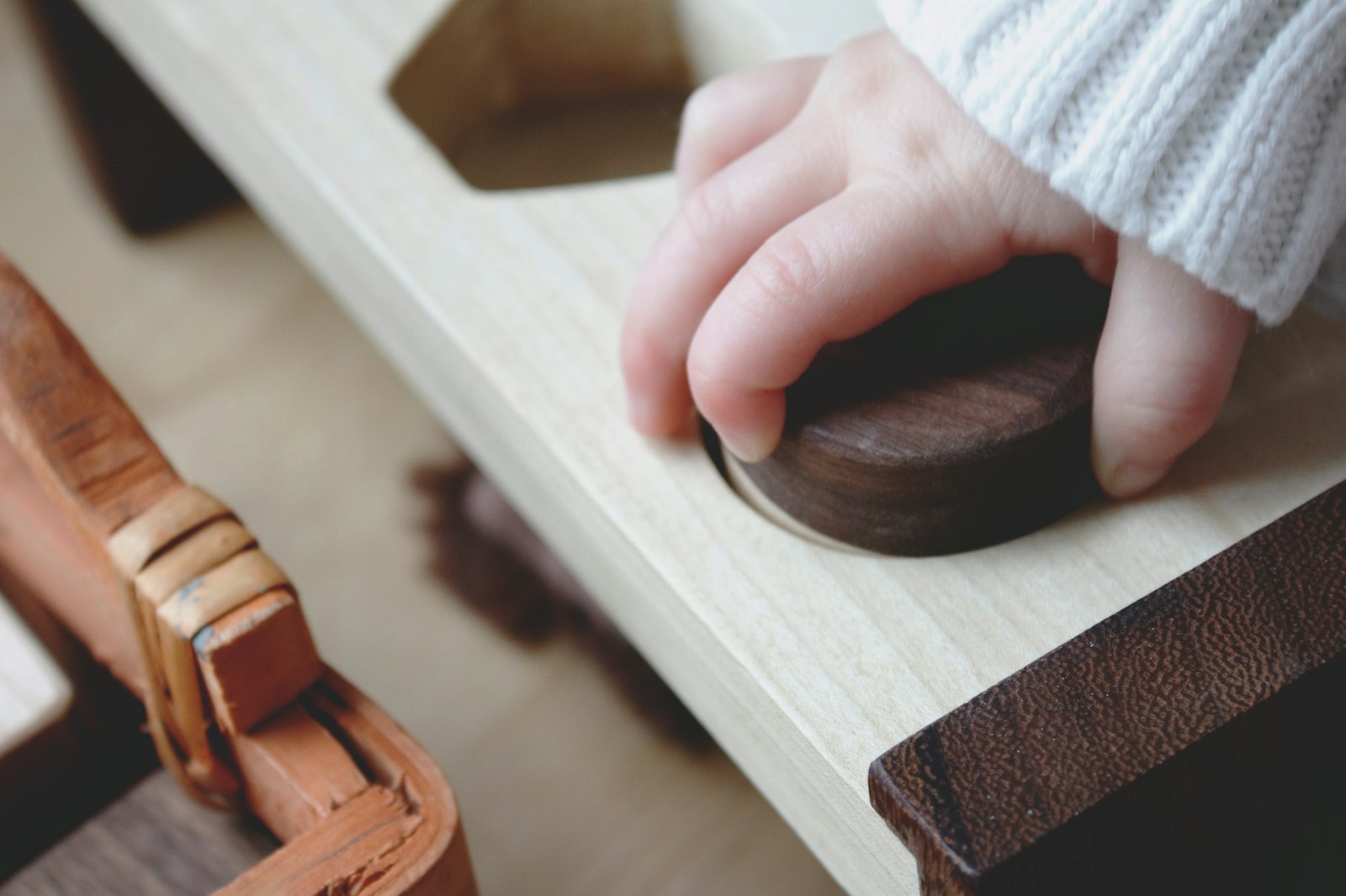 A baby hand resting on a smooth wooden Montessori sorter, in soft natural light.