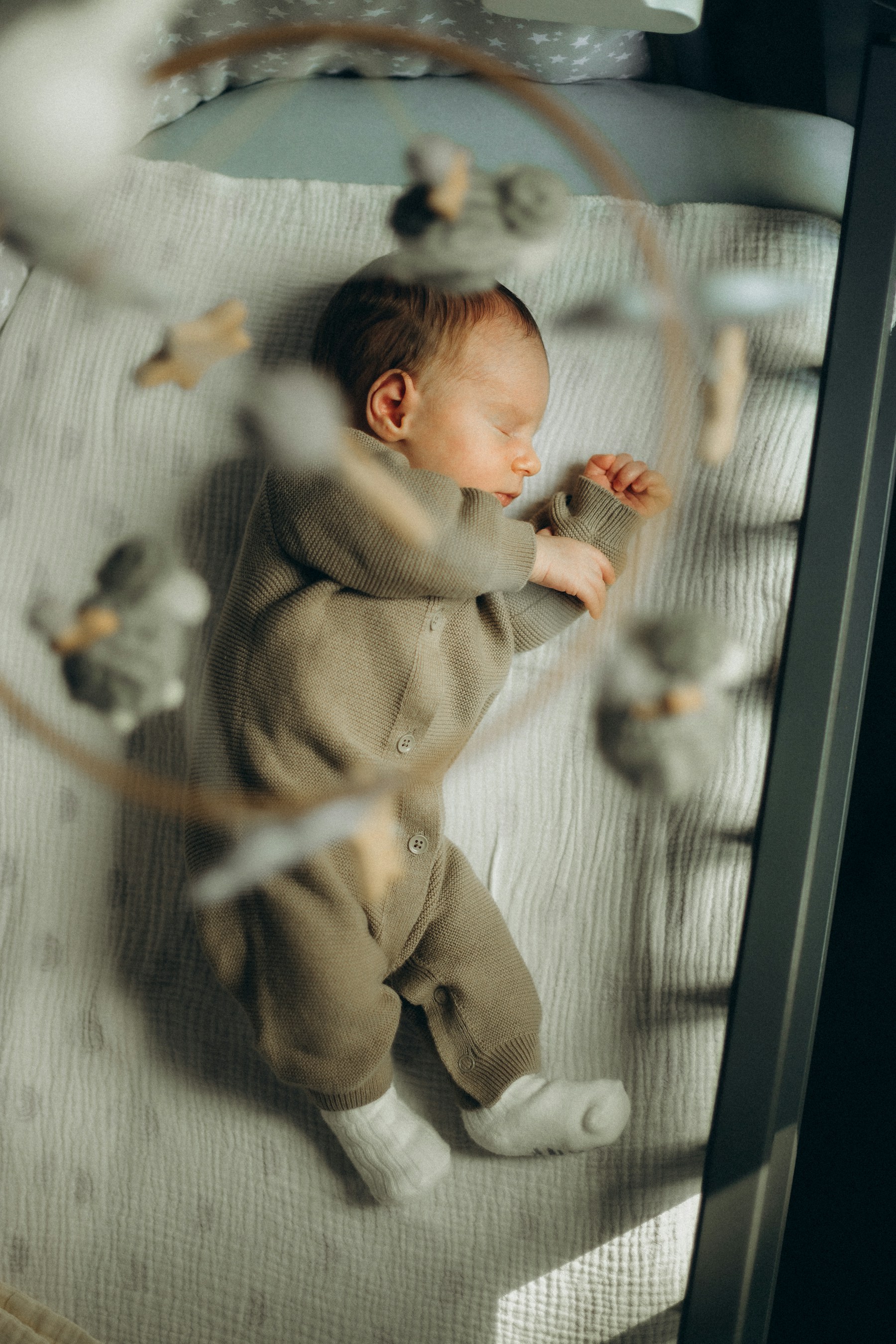 A newborn sleeping peacefully in a crib beneath a soft mobile, photographed by Ana Curcan on Unsplash.