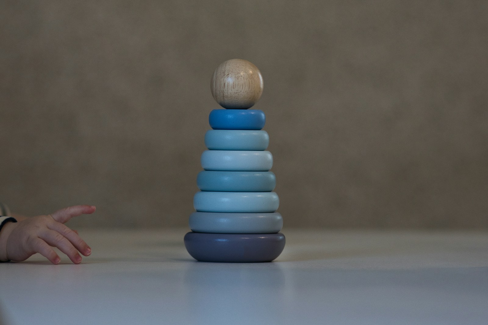 A tower of blue wooden stacking rings on a table, a babys hand reaching toward it.