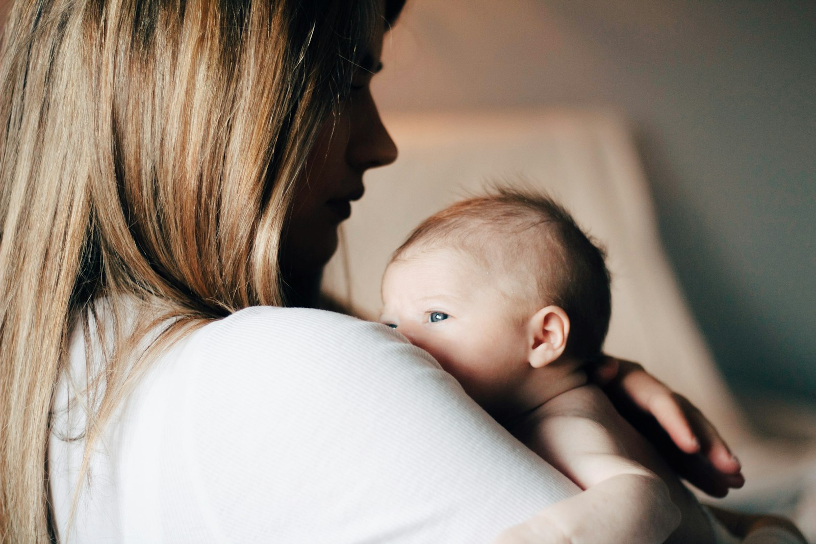 A mother in a white shirt cradling her newborn close.