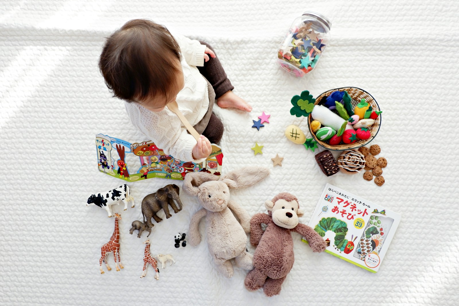 Overhead view of a baby on a soft mat surrounded by wooden animals, a basket of felt food, and books.